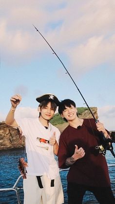 two young men standing next to each other while holding fishing rods