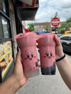 two people holding up pink drinks in front of a building