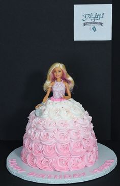 a barbie doll sitting on top of a pink and white cake