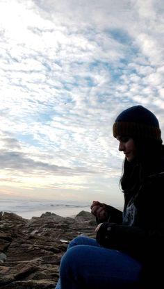 a woman sitting on top of a rocky beach next to the ocean