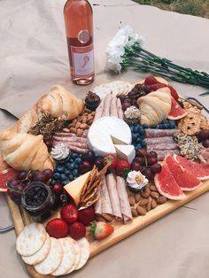 a platter with cheese, crackers, fruit and bread on it next to a bottle of wine