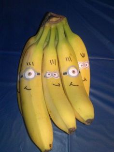 three bananas with faces drawn on them sitting on a blue cloth covered tableclothed surface