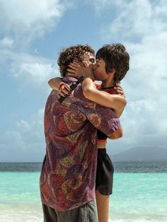 two people are hugging on the beach while one person is standing in front of them