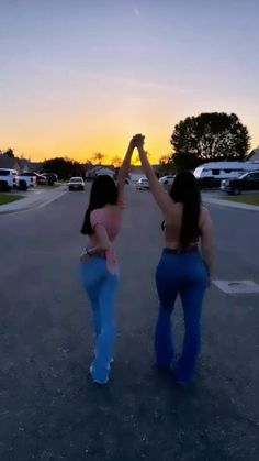 two women standing in the middle of a parking lot holding their hands up to the sky