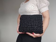 a woman holding a black crochet purse in her hands and wearing a white blouse