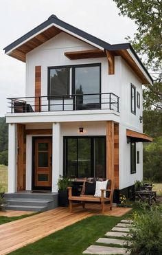 a white house with wood accents and black trim on the front porch, sitting in grass next to a wooden deck