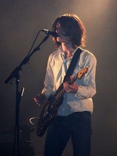 a man with long hair playing guitar in front of a microphone on stage at a concert