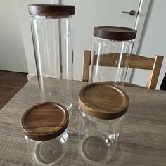 two glass jars with wooden lids sit on a table next to a chair and door