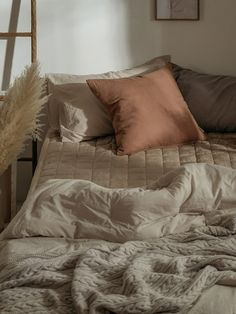 an unmade bed with pillows and blankets on it, next to a ladder in the corner