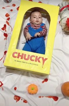 a baby in a chucky box laying on a bed with oranges around it