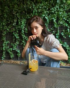 a woman sitting at a table with a camera in front of her and a glass of orange juice