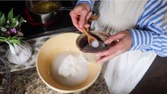 a person in an apron is stirring something into a bowl with a spoon and wooden spoon