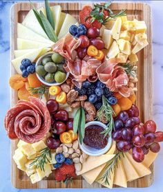 an assortment of cheeses, fruits and meats arranged on a wooden platter