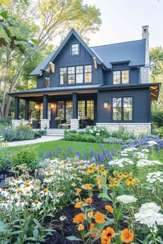 a large blue house with lots of flowers in the front yard and landscaping around it