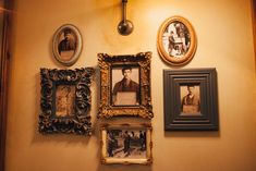 several framed pictures hang on the wall next to two lamps and an old fashioned clock