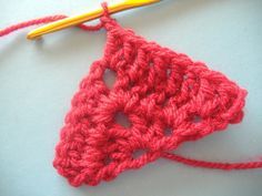 the crochet triangle is being worked on with a yellow knitting needle and yarn