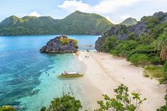 a boat is docked on the beach near some rocks and water with green trees in the foreground