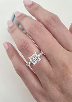 a woman's hand with a diamond ring on top of her finger and the other hand holding an engagement ring