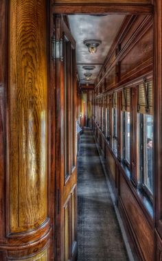 a long hallway with wood paneling and wooden doors leading to another room in the building