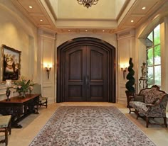 a large foyer with an ornate rug and chandelier above the entrance door is flanked by two chairs