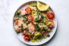 a white plate topped with meat and veggies next to a slice of lemon