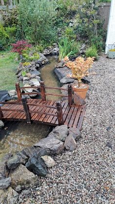 a wooden bridge over a small stream in a garden with rocks and plants around it