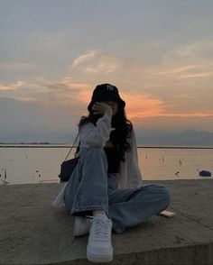 a woman sitting on the beach with her head in her hands while she is talking on her cell phone