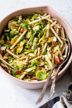 a bowl filled with salad next to a fork and spoon on top of a table