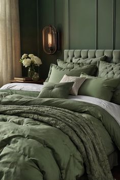 a bed with green comforter and pillows in a room next to a table with flowers on it