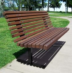 a wooden park bench sitting on top of a cement slab next to a grass covered field