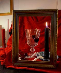 a candle is lit next to an empty wine glass and cherries on a table