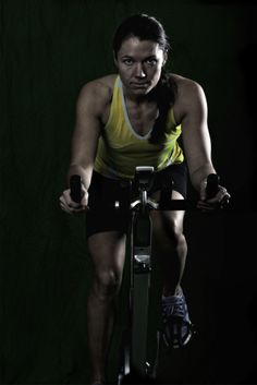 a woman on a stationary bike in the dark with her hand on the handlebars