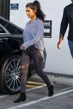 a woman walking across a parking lot next to a black car