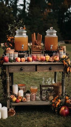 an old wooden table with apples and candles on it, surrounded by fall decorations in the grass