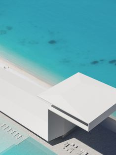 an aerial view of a white building next to the ocean with blue water in the background