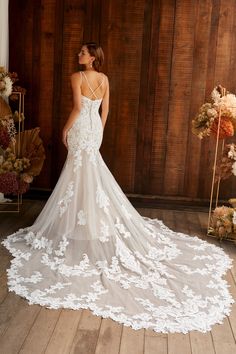 a woman in a white wedding dress standing on a wooden floor with flowers behind her