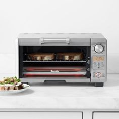 an open toaster oven sitting on top of a counter next to a plate of food