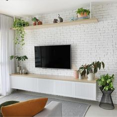 a flat screen tv mounted on a white brick wall in a living room with potted plants