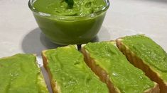 two pieces of bread with green spread on them next to a small bowl of pesto