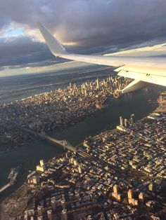 the wing of an airplane flying over a large city and river under a cloudy sky