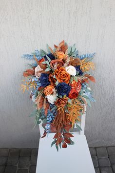 an arrangement of flowers is displayed on a white stand in front of a gray wall