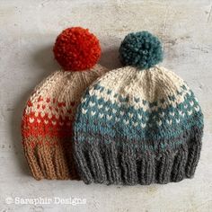 two knitted hats sitting next to each other on top of a white surface with red and blue pom poms