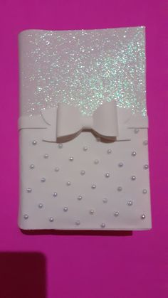 a white gift box with silver sequins and a bow on the front, against a pink background