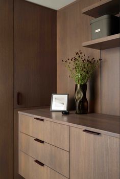 a vase filled with flowers sitting on top of a wooden dresser next to a shelf