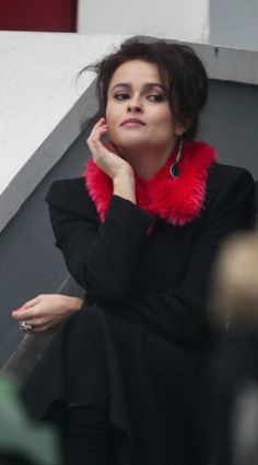 a woman sitting down with her hand on her chin and wearing a red scarf around her neck