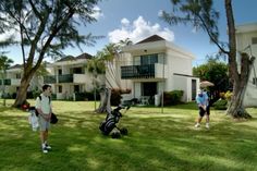 two men are standing in the grass with golf gear and an umbrella near some apartment buildings