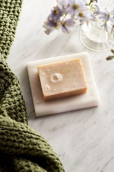 a square soap bar sitting on top of a white plate next to a green scarf