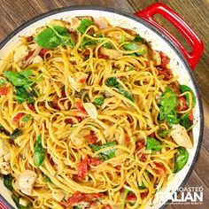 pasta with chicken, spinach and tomatoes in a red skillet on a wooden table