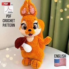 an orange crocheted stuffed animal holding a piece of food in its paws and standing on top of a table