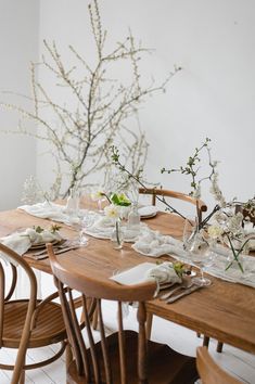 a wooden table topped with lots of white plates and place settings next to a vase filled with flowers